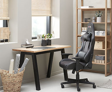 Schreibtisch mit Platte in Holzoptik und schwarzen Beinen, daneben schwarzer Bürostuhl und hohes Regal aus Holz