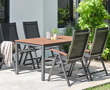 Eckiger Gartentisch mit schwarzen Beinen und dunkler Holztischplatte und vier hohe Positionsstühle in derselben Optik