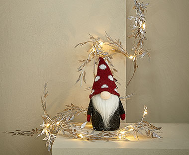 Weihnachtswichtel mit roter Mütze dekoriert mit einer Lichterkette mit Zweigen