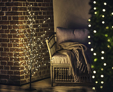 Sapin de Noël aux branches lumineuses près d'un fauteuil au coin de la pièce