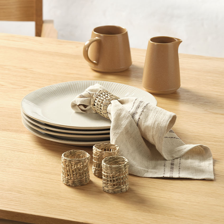  Piatti bianchi a coste, brocca del latte, tovagliolo di stoffa e anelli per tovaglioli sulla tavola da pranzo.