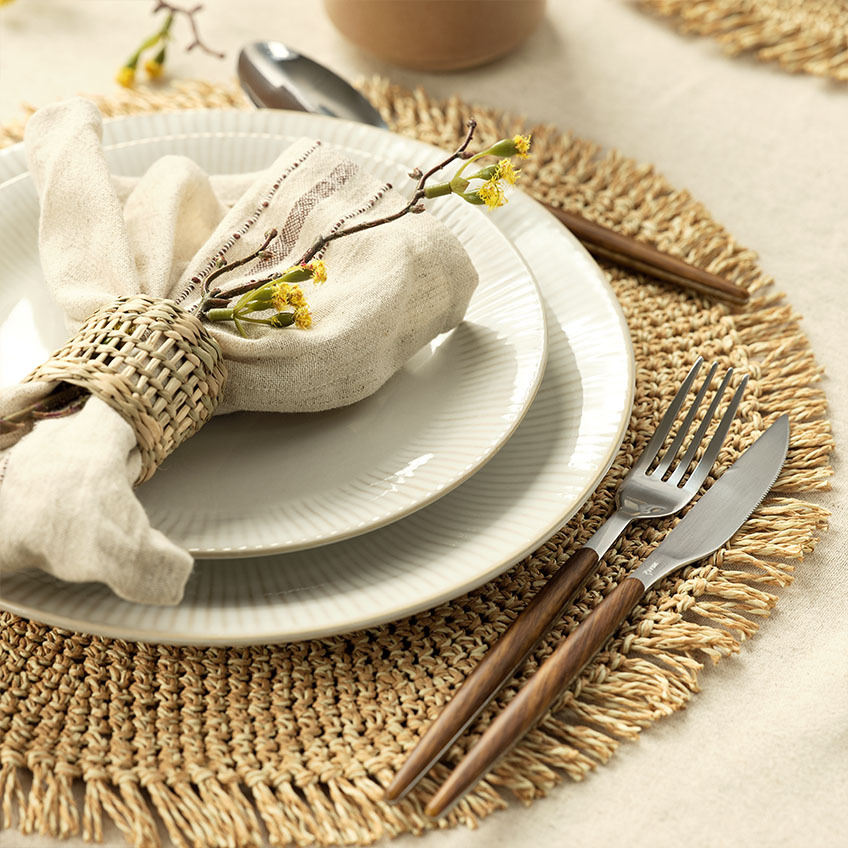 Assiette blanche à côtes, serviette en tissu, anneau de serviette, ensemble de couverts et set de table.
