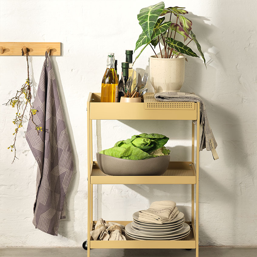 Vaisselle sur un chariot dans la cuisine avec des assiettes, un grand bol, un ensemble de couverts et une plante artificielle