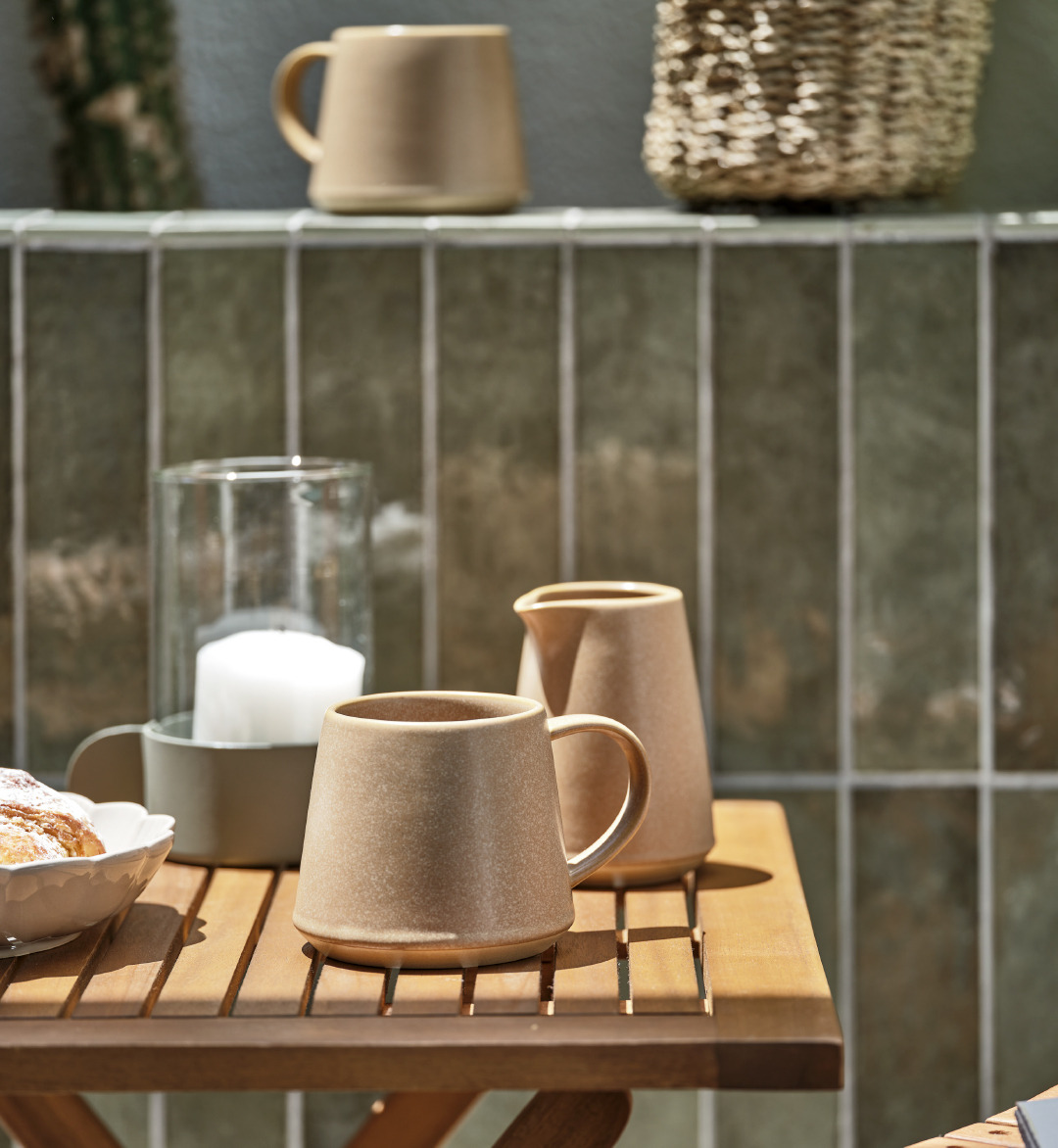 Lattiera e tazza in color marrone e stile rustico e lanterna in vetro ed acciaio su tavolo ben allestito