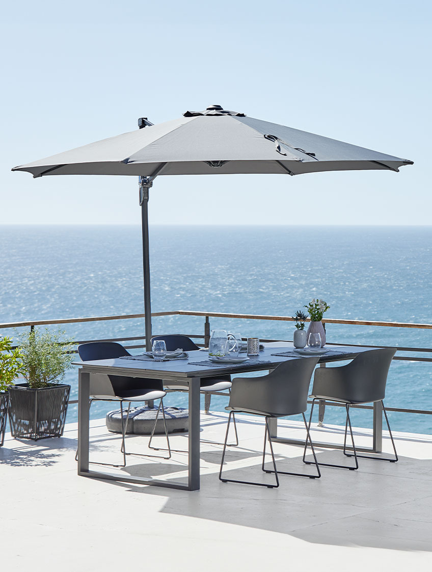 Grosser hängender Sonnenschirm und Gartentisch und Stühle auf der Terrasse am Meer