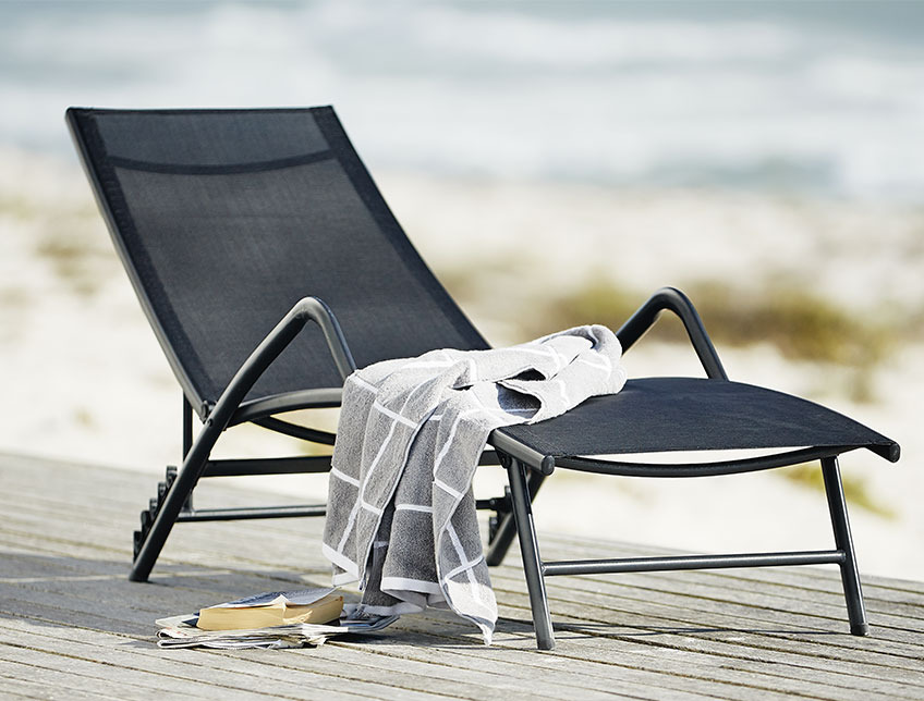 Schwarze Sonnenliege mit Armlehnen auf einer Terrasse beim Strand